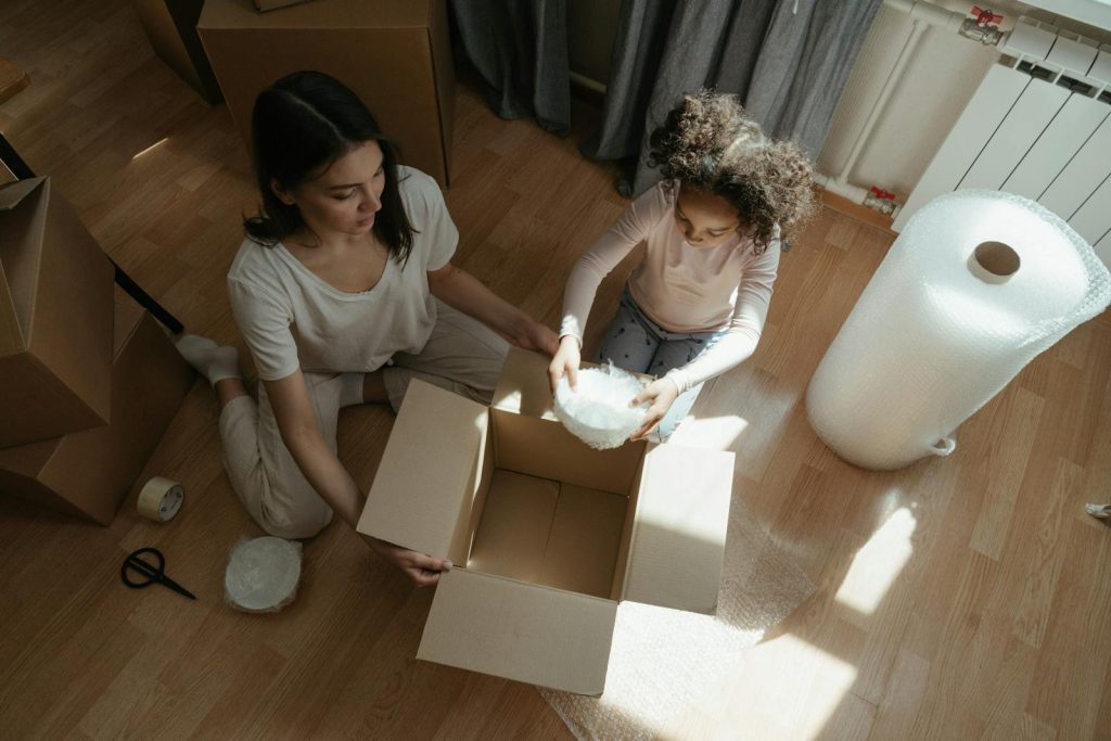 A mother and daughter packing with cardboard boxes and bubble wrap indoors.